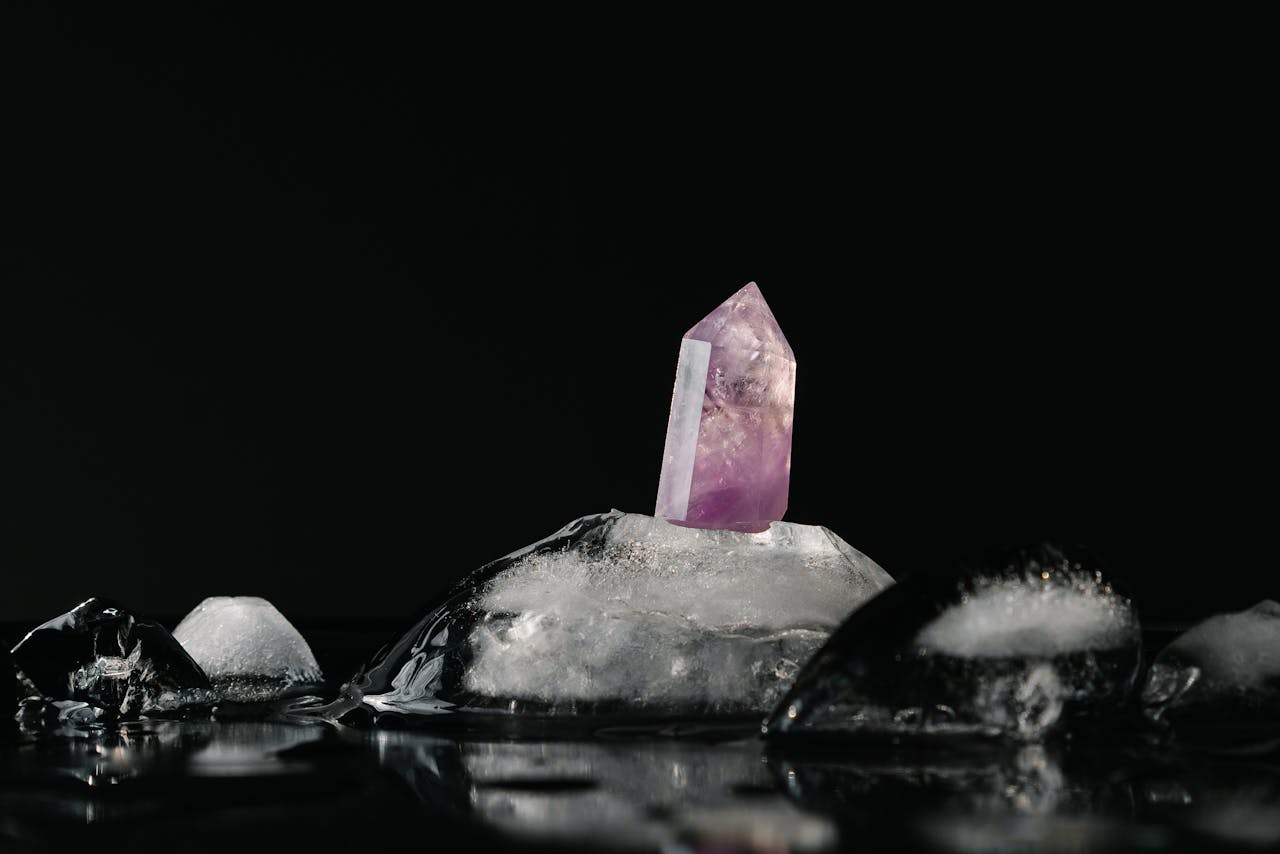 A vivid purple amethyst crystal surrounded by melting ice on a reflective black surface.