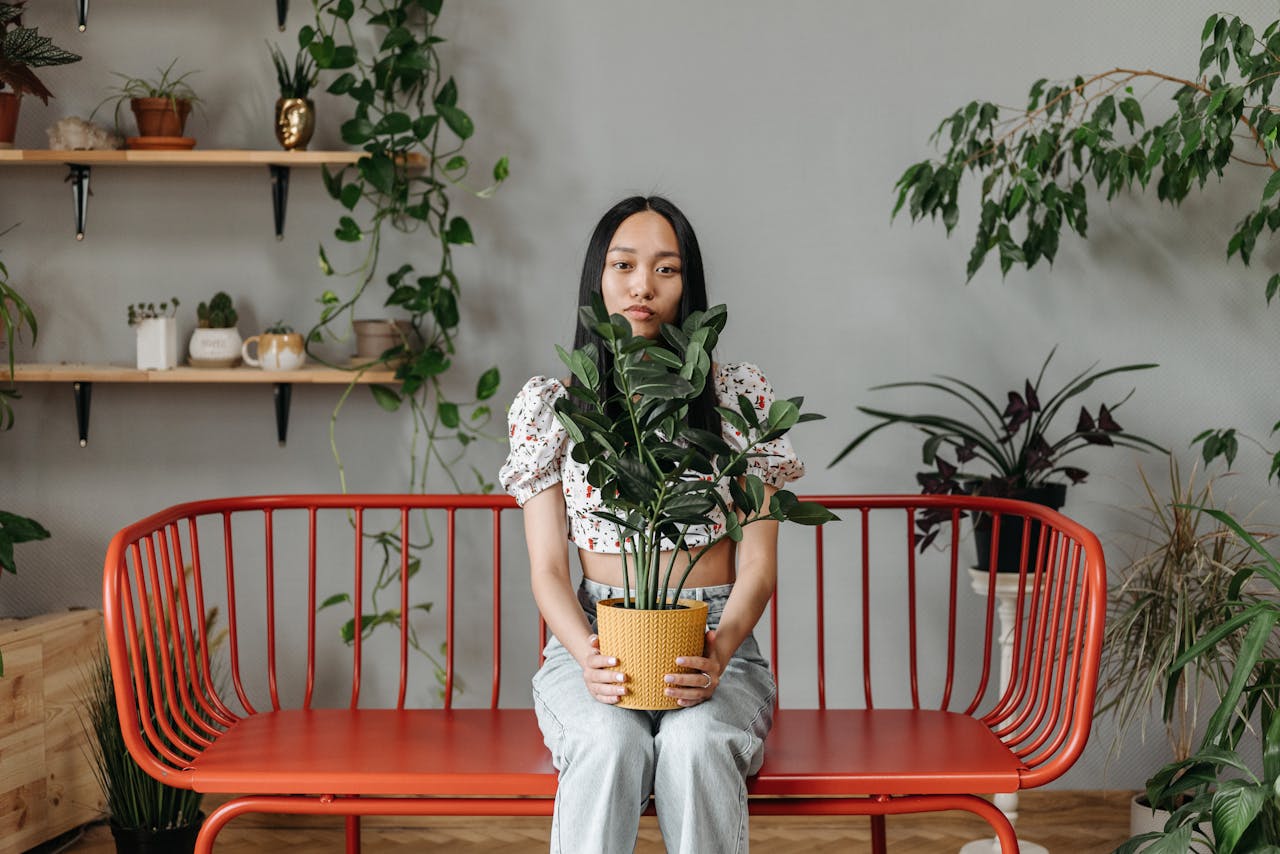Woman caring for plants indoors sitting on a decorative red bench.